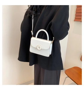 Side view of model carrying a white leather crossbody bag with golden metal ring buckle