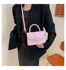 Detail of a light pink leather square bag with a prominent golden circular metal buckle