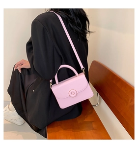 Detail view of pink leather crossbody bag with circular metal clasp and adjustable strap