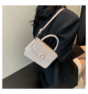 Detail view of a cream white crossbody square bag with a round buckle and top handle