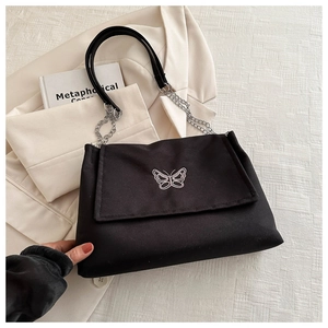 Détail de la broderie papillon et de la chaîne en argent sur un sac à bandoulière noir