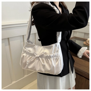 Close-up of white pleated satin underarm bag with bow detail worn by a model