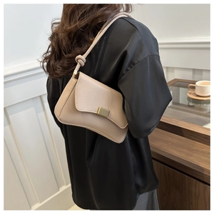 Chic beige shoulder bag with gold clasp and knotted strap shown in an elegant setting
