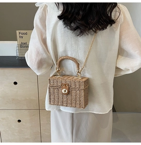 Detail of a rectangular straw woven handbag featuring a metal chain and turn-lock closure