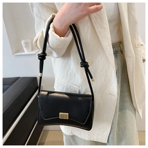 Close-up of black leather crossbody bag with gold vertical metal buckle and knotted strap