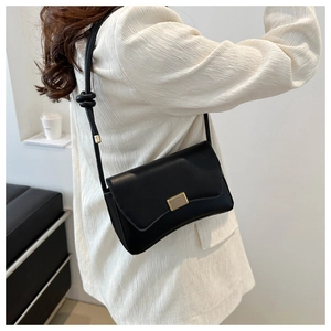 Black minimalist flap crossbody bag with gold textured lock and knotted shoulder strap