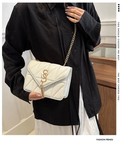 Detail of white quilted crossbody bag with golden S logo and chain strap on model