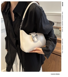 Gros plan du sac besace beige avec nœud argenté et détails de chaîne métallique