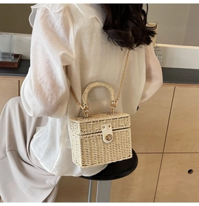 Detail of cream woven straw box bag with gold chain strap on a female model