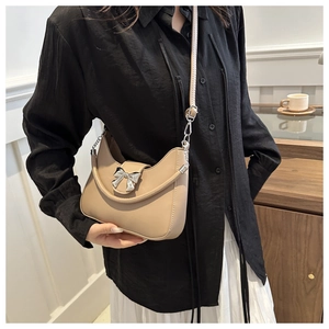 Sac selle beige en demi-lune avec nœud argenté et bandoulière chaîne sur modèle