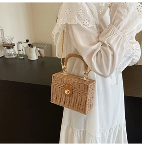 Detail of beige straw box bag showing woven texture, leather buckle, and gold chain strap