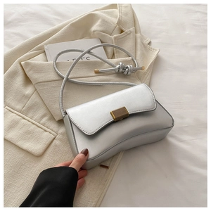 Detail of silver metallic shoulder bag with gold vertical lock on a beige blazer
