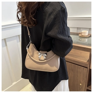 Détail du sac à bandoulière beige avec nœud argenté et chaîne, présenté sur un mannequin