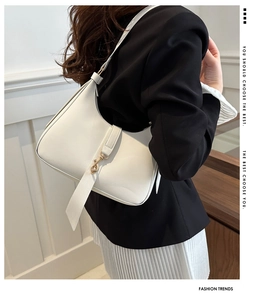 Close-up of white crescent underarm bag with gold metal hardware on model in a blazer