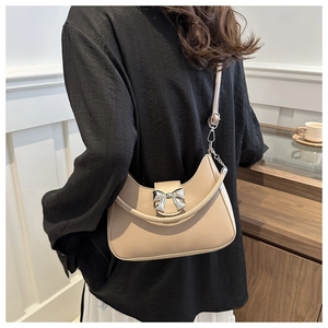 Sac bandoulière beige en similicuir avec boucle nœud argenté porté par un mannequin chic