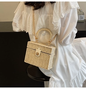 Detail of cream rectangular straw bag with gold chain strap and metallic twist lock