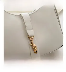 Macro shot of gold metal buckle and neat stitching on white leather baguette bag