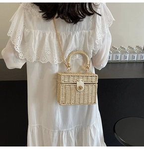 Detail of woven straw box bag with white leather handle and gold chain strap