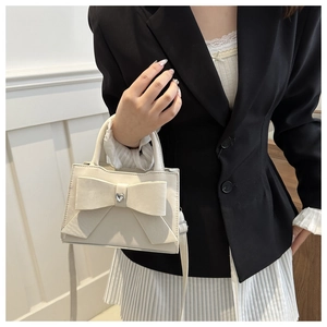 Détail du sac à main crème avec nœud décoratif, strass en cœur et finition cuir