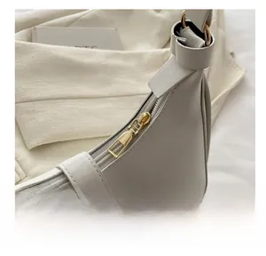 Detailed close-up of the smooth gold-toned metal zipper on a cream white crescent bag