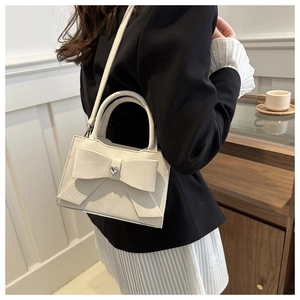 Détail du sac à main crème avec nœud décoratif, strass en cœur et poignée haute