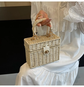 Detailed close-up of straw woven handbag with white leather trim and gold metal twist lock