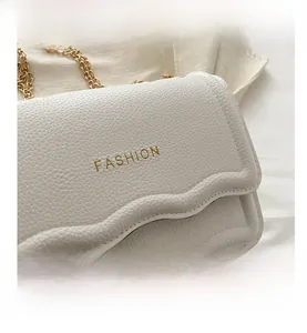 Détail d'un sac à main en cuir blanc aux bords ondulés et chaîne dorée