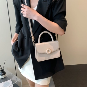 Minimalist beige crossbody bag with circular gold buckle and top handle worn by model