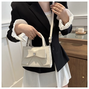 Détail du sac crème avec grand nœud et strass en forme de cœur dans un décor de café chic