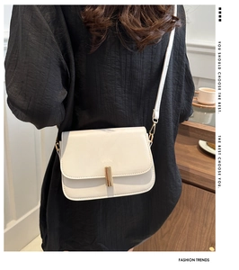 Detail view of a cream square crossbody bag with gold metallic buckle and thin leather strap