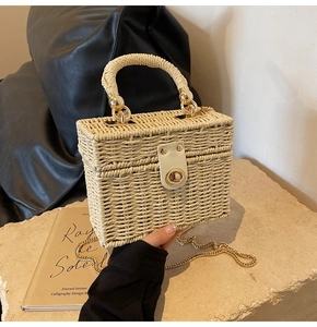 Close-up of woven straw box bag with gold metal clasp and detachable chain strap
