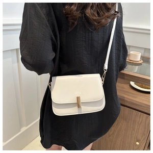 Detail view of cream flap crossbody bag with gold cylindrical lock and slim strap