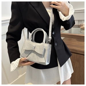 Détail du mini sac gris argenté avec nœud et strass cœur, porté sur une tenue élégante