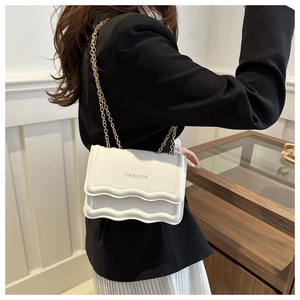 Close-up of white textured leather crossbody bag with scallop trim and gold chain strap