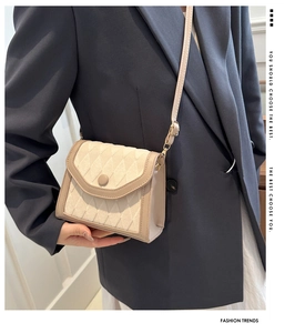 Detail of a cream quilted crossbody bag with diamond stitching on a model outfit