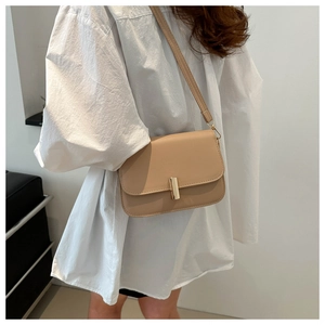 Detail view of stylish beige leather crossbody bag with golden metal buckle on a model