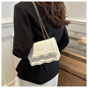 Detail of white leather chain bag featuring scalloped edges and gold metal strap detail
