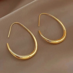 Gros plan de boucles d'oreilles gouttes en titane doré poli sur un fond en tissu sombre