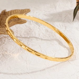 Fashionable gold titanium steel bangle with geometric diamond pattern on white paper background