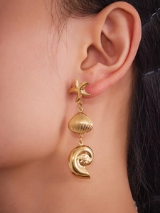 Detailed view of gold stainless steel shell and starfish drop earrings on a model