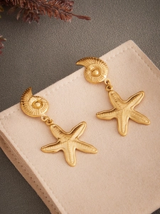 Close-up of gold conch and starfish drop earrings with fine textured metal details