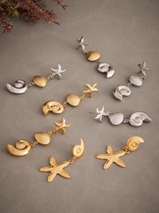 Detailed flat lay of stainless steel seashell and starfish dangle earrings in gold and silver