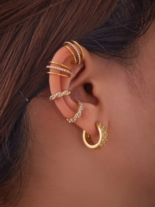 Primer plano de pendientes ear cuff dorados con circonitas apilados en la oreja
