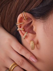 Primer plano de pendientes de cartílago y anillos dorados con circonitas para mujer