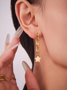 Close-up of gold chain earrings with star pendants and a hollow woven ring on model