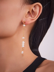 Close-up of gold chain earrings with five white dangling pearls worn by a model