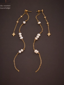 Detail of gold star tassel earrings with irregular pearls on a brown textured background