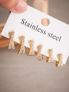 Détail de trois paires de boucles d'oreilles en acier doré en forme de X avec zircons