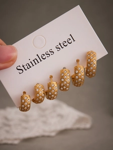Makro-Detail von drei Paar goldenen Edelstahl-Ohrringen mit CNC-Gittermuster und Zirkonia