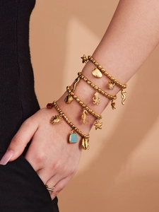 Detalle de pulsera multicapa dorada con colgantes de caballito de mar y estrella de mar